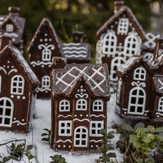 A collection of ceramic gingerbread-style houses with white decorative patterns, positioned on a surface with artificial snow, likely part of Christmas decorations.
