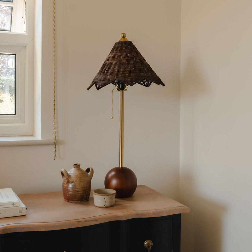 Lamp on a wooden surface next to a window with a plaid curtain.
