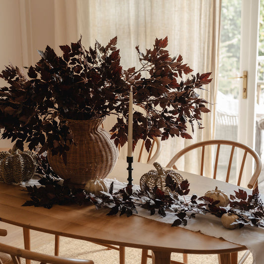 Dining room with a wooden table, chairs, and decorative elements including a vase with dark leaves.
