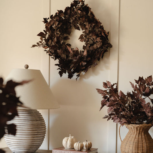Decorative setting with a wreath, pumpkins, and books on a wooden surface.